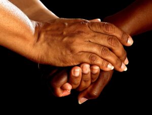How can caregivers ask for help? This is an image of two sets of African American hands holding each other on a black background.