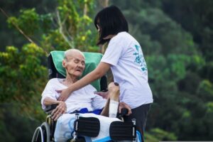 Young woman Caregiver helping elderly man in wheelchair. Family can do the same with or without Personal Care Agreements