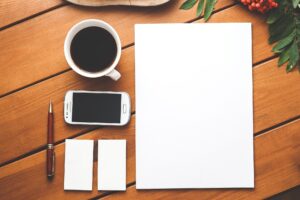 Coffee, a notepad, sticky notes, and a smartphone on a desk to help one get organized.