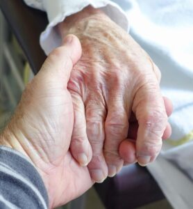 Person holding an elderly woman's hand demonstrating compassion and caring