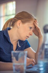 Woman in a ponytail holding her head in her hand looking worried and stressed woman because of caregiver burnout
