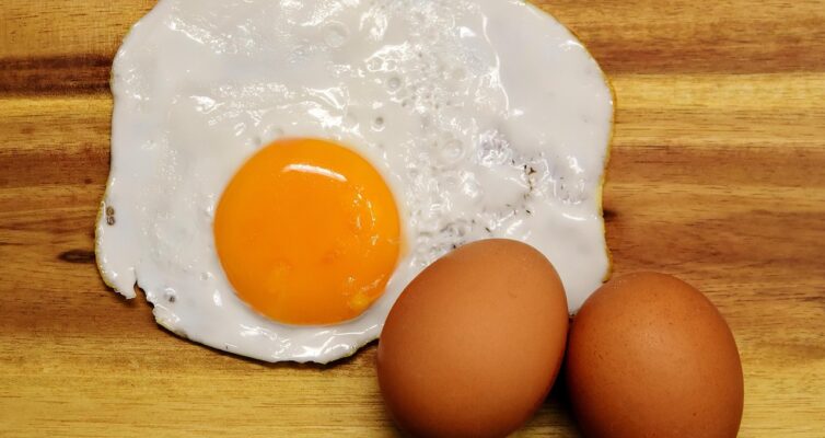 two eggs in their shells and one fried egg on a cutting board